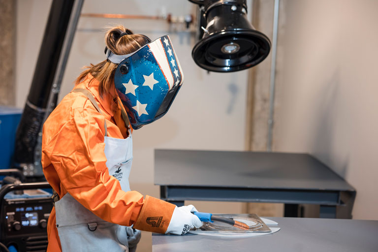 Caroline Sheridan practices proper posture and PPE wear while using a MIG welder