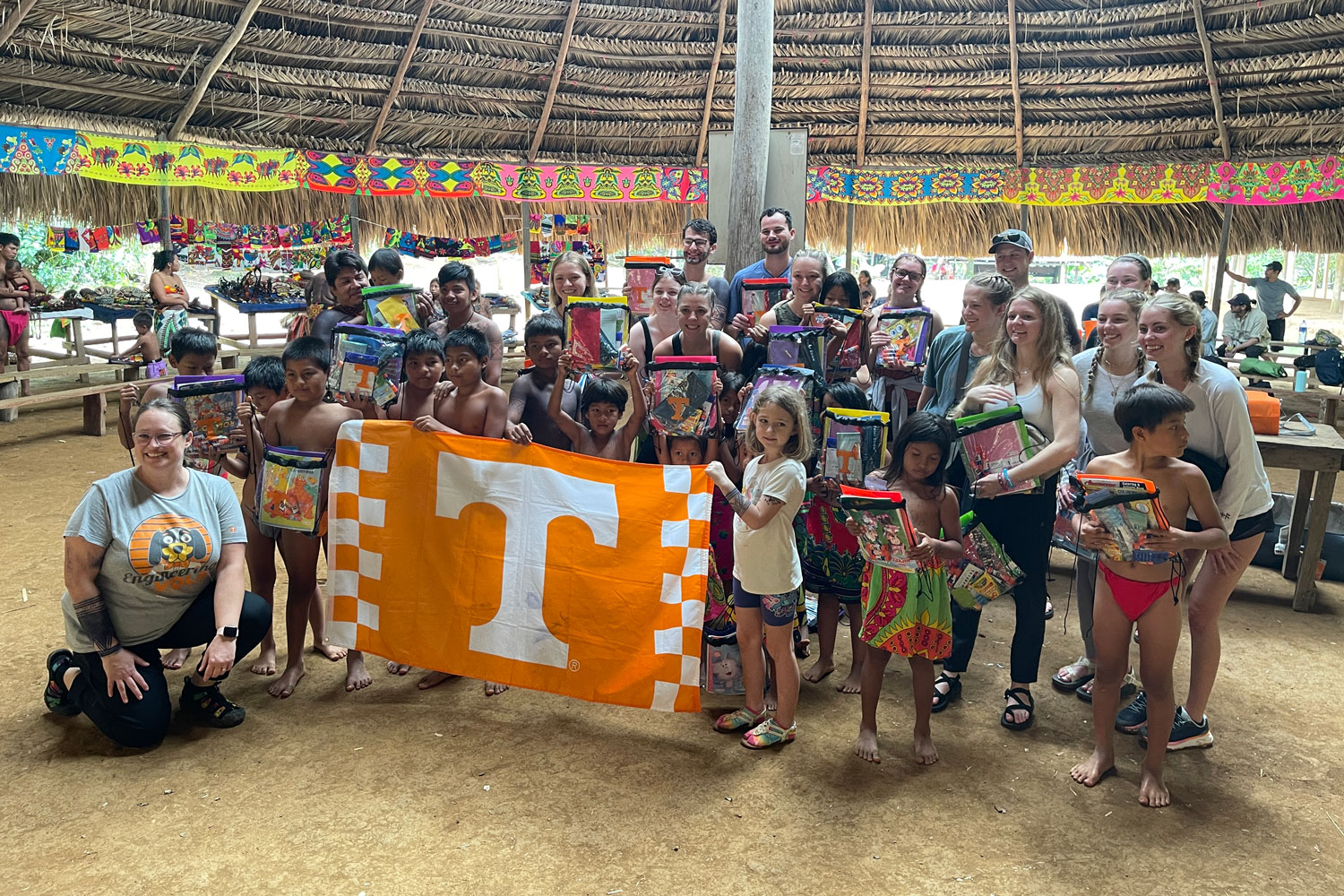 Students posing with children with the UT flag under straw hut