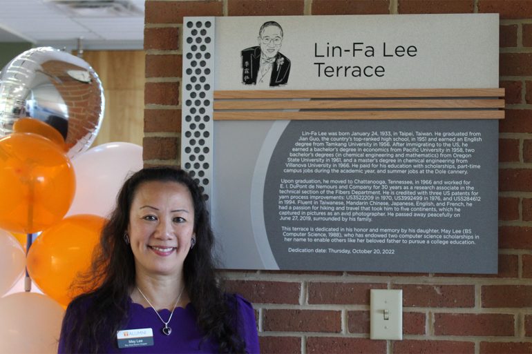 May Lee standing in front of a dedication plaque for Lin-Fa Lee Terrace.
