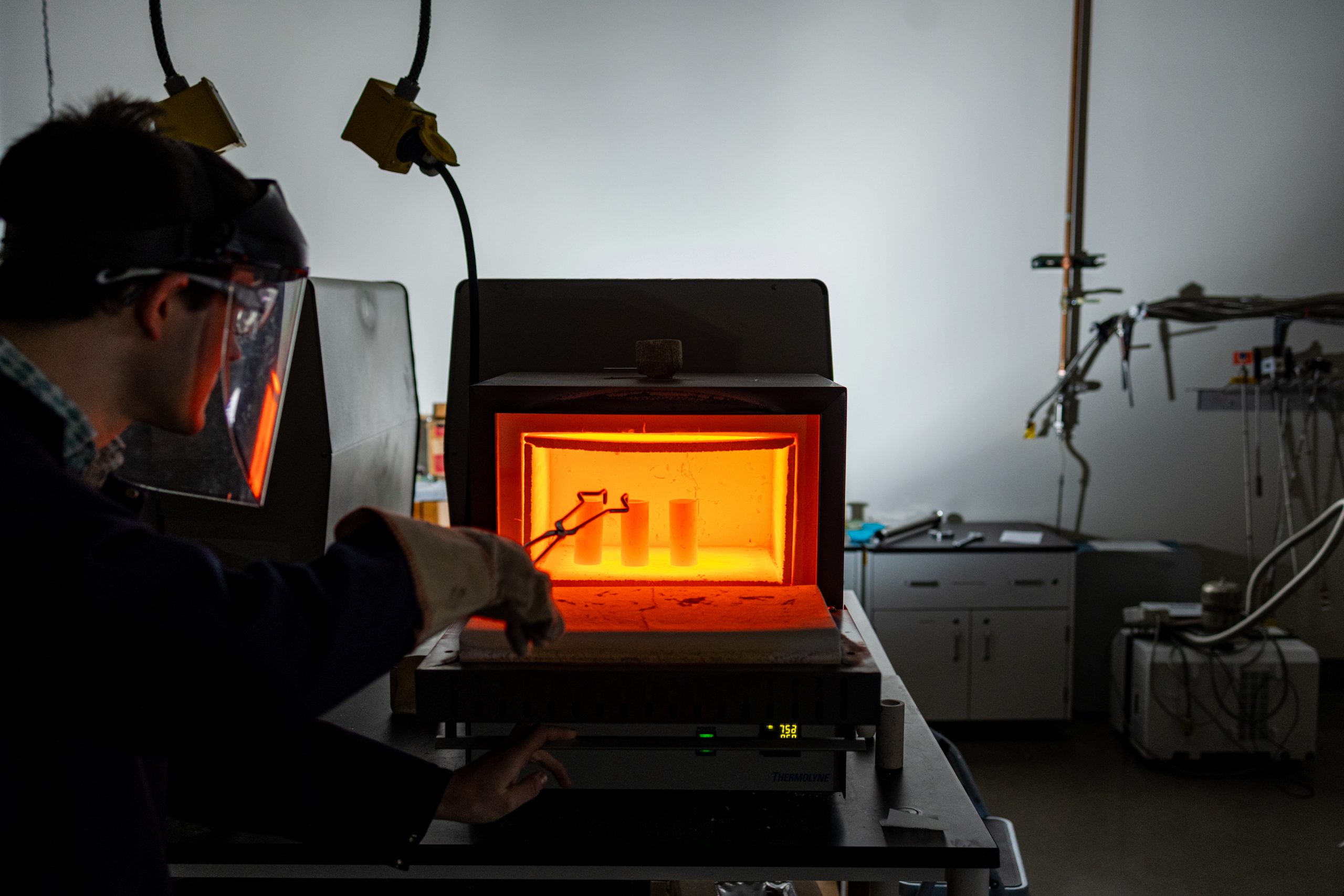 William Meier putting materials in an oven while wearing protection in a lab