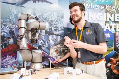 Male student smiling and holding component of interdisciplinary student design project