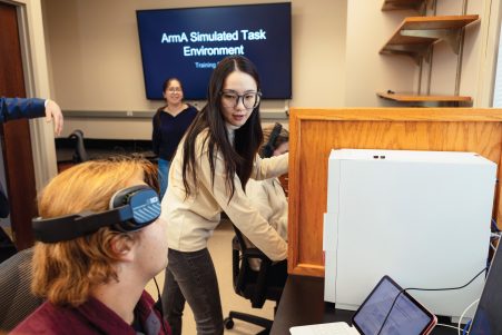 A female student talking to another student with headphones resting on his temples