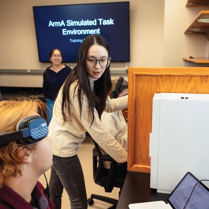 A female student talking to another student with headphones resting on his temples