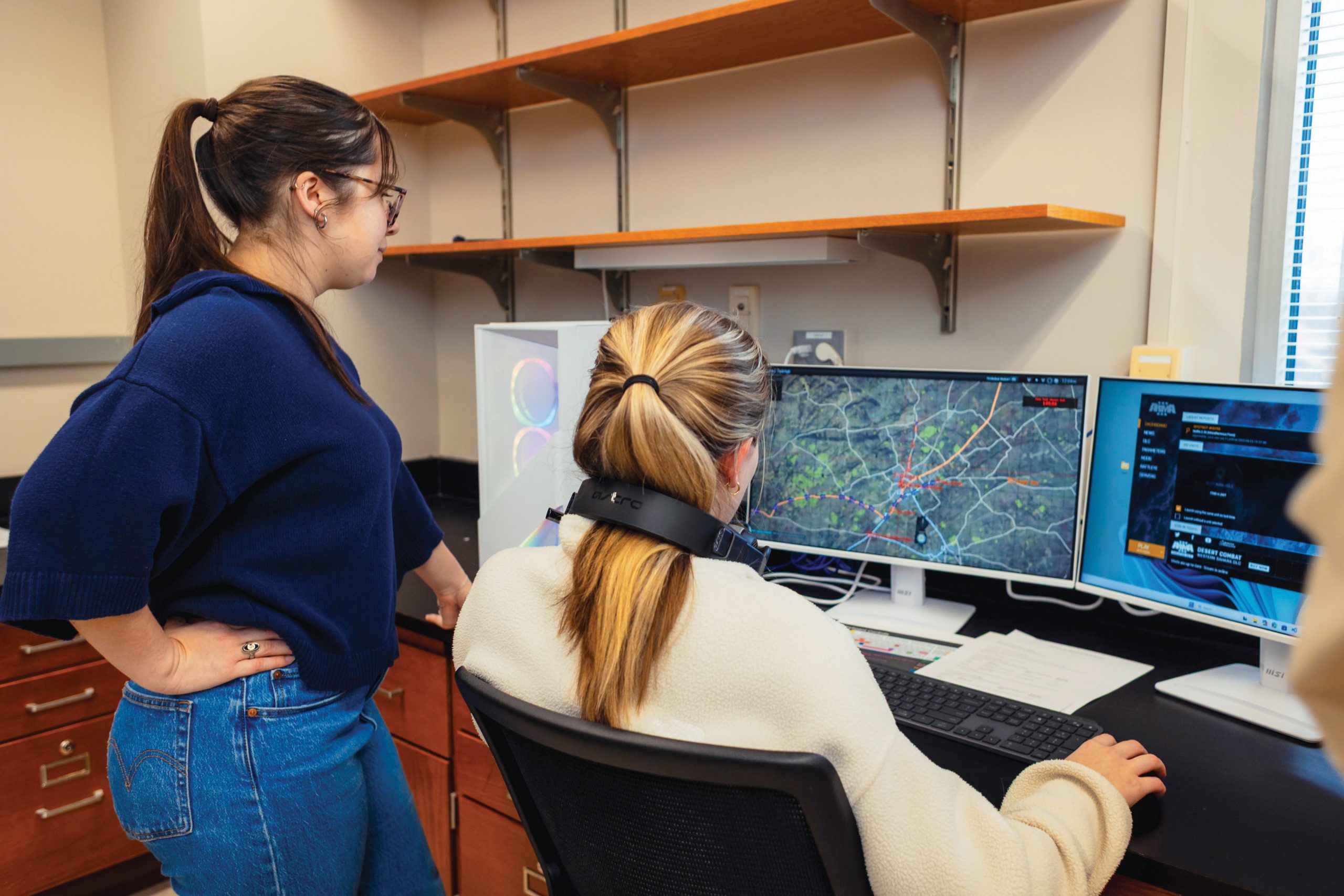 Two women looking at a computer screen with a geographic map and colorful road lines