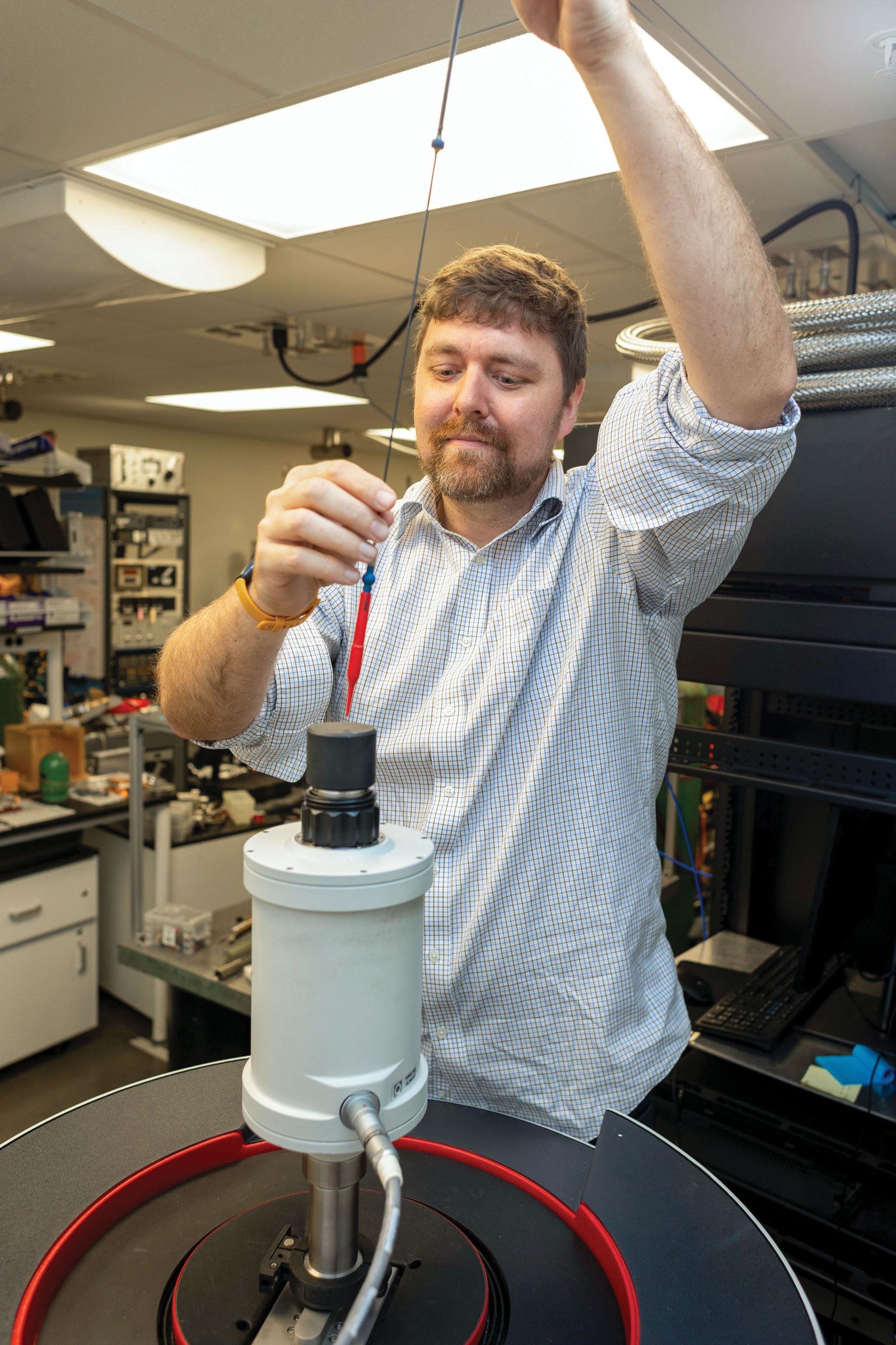 Professor Dustin Gilbert holding up a long string-like mechanism above a machine.
