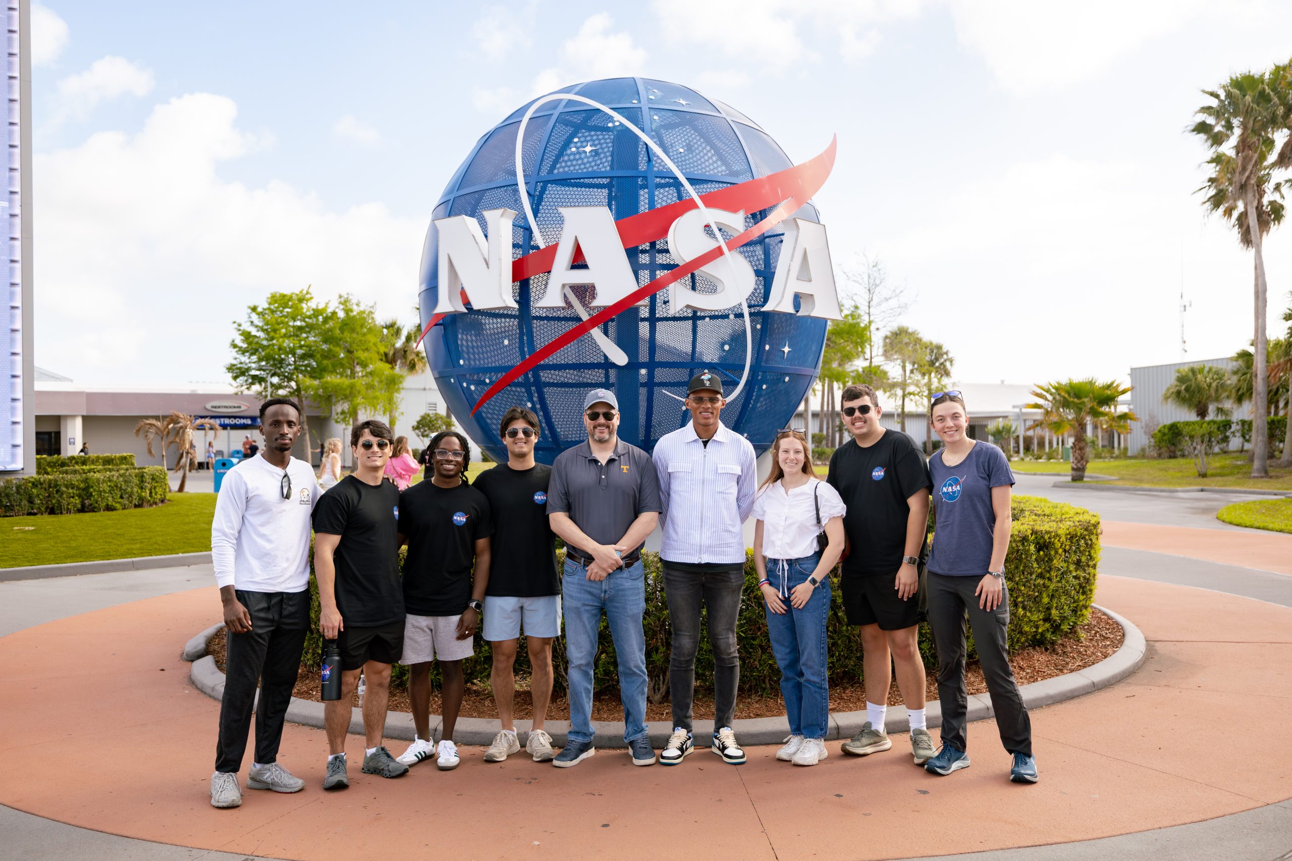 Mechanical and aerospace engineering students and Dean Matthew Mench stand in front of a large spherical NASA sign