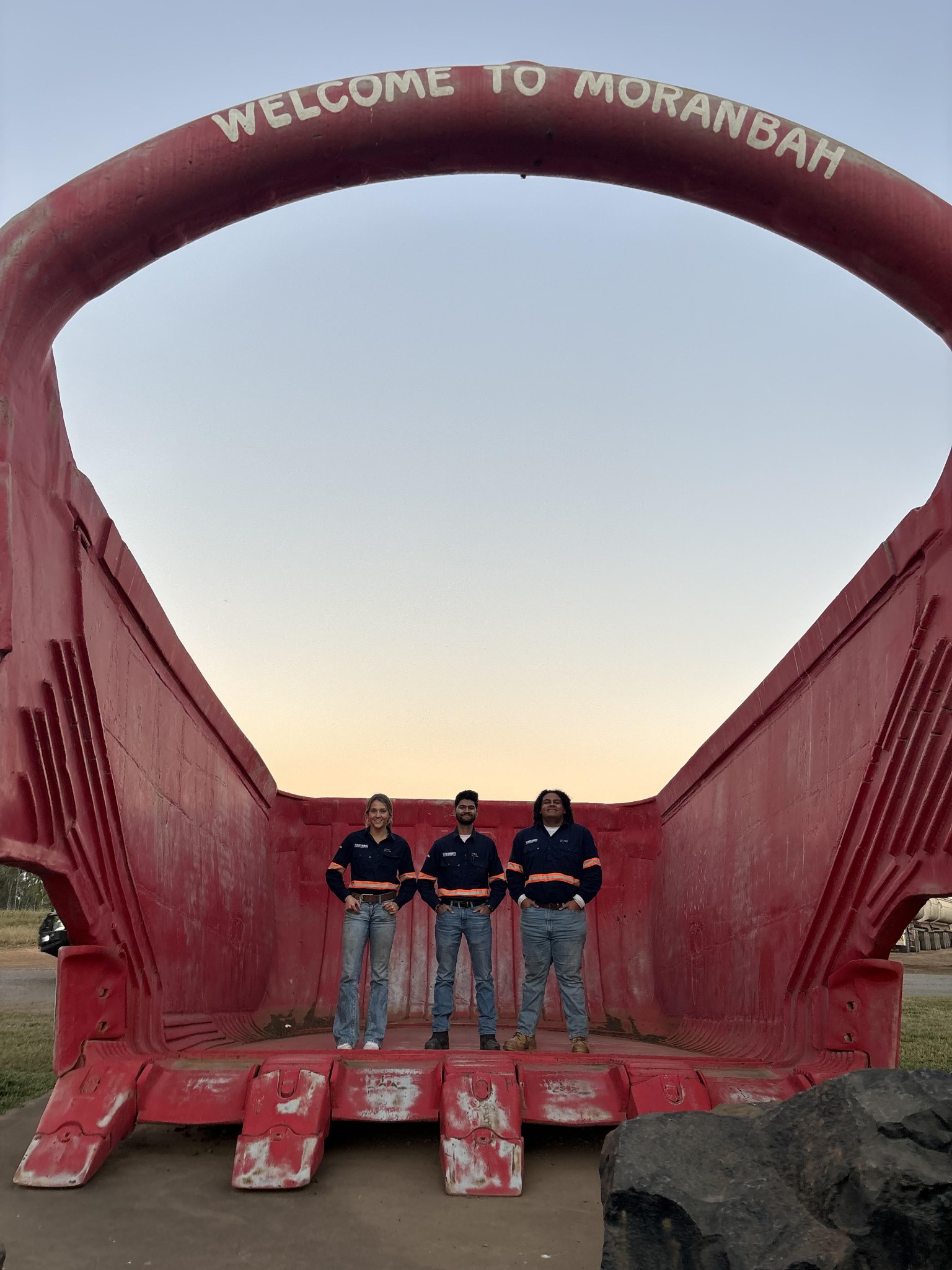 Three group members standing in a large red container labeled 'Welcome to Moranbah'