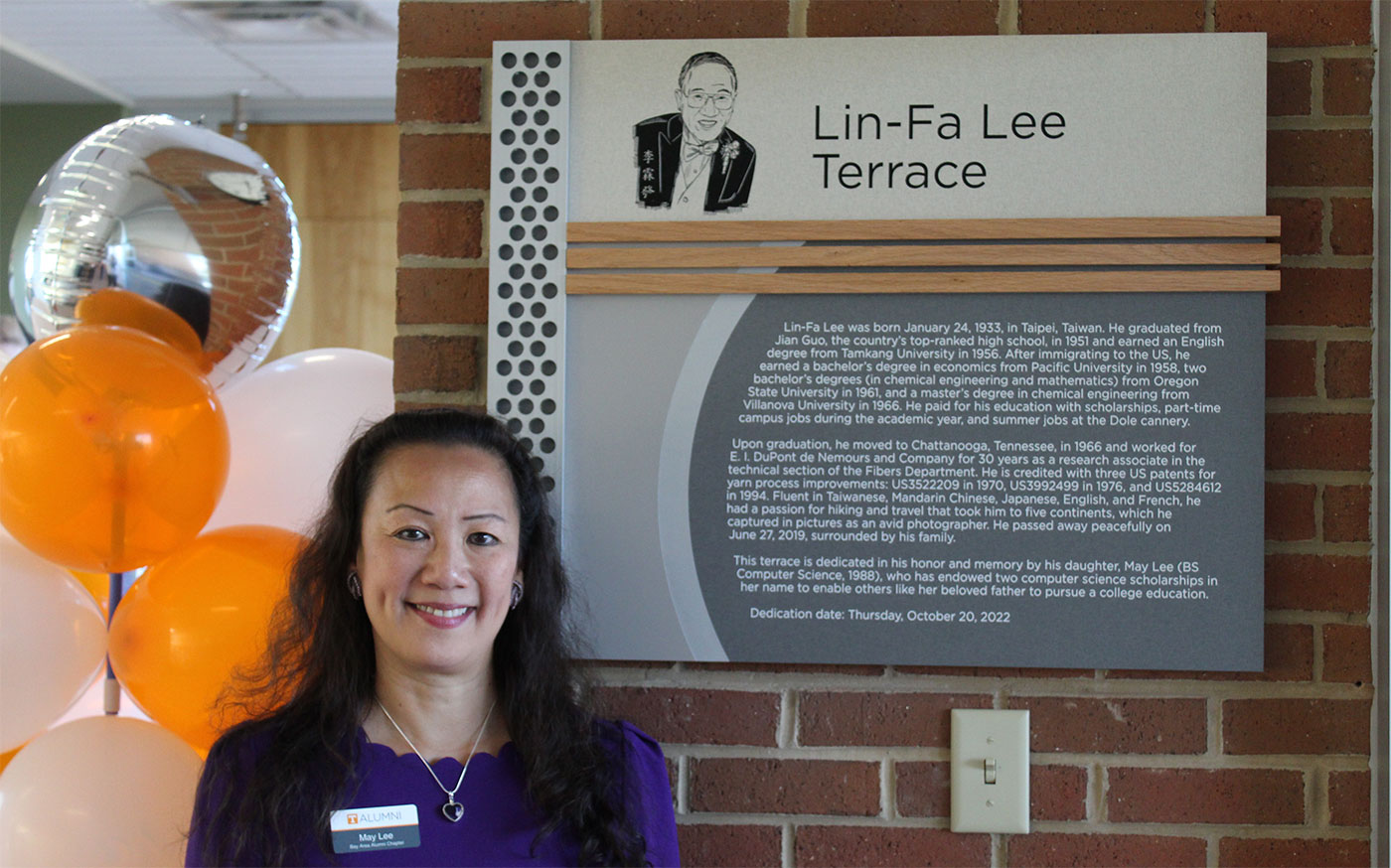 May Lee standing in front of a dedication plaque for Lin-Fa Lee Terrace.