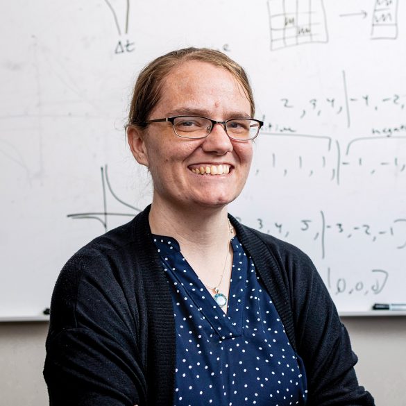 Katie Schuman stands in front of a dry erase board with formulas written on it.