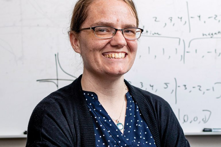 Katie Schuman stands in front of a dry erase board with formulas written on it.